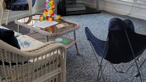 A living room with a TV, wicker furniture, a glass coffee table, and a view of the outside. - Immaculate Cottage, Huge Deck And Great Back Yard For All Your Yard Games. (Middletown)