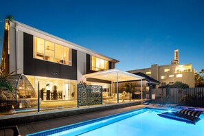 Una casa moderna con piscina, mobiliario exterior y un patio cubierto.