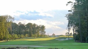 Un campo de golf con un edificio a lo lejos, rodeado de árboles y césped cuidado.