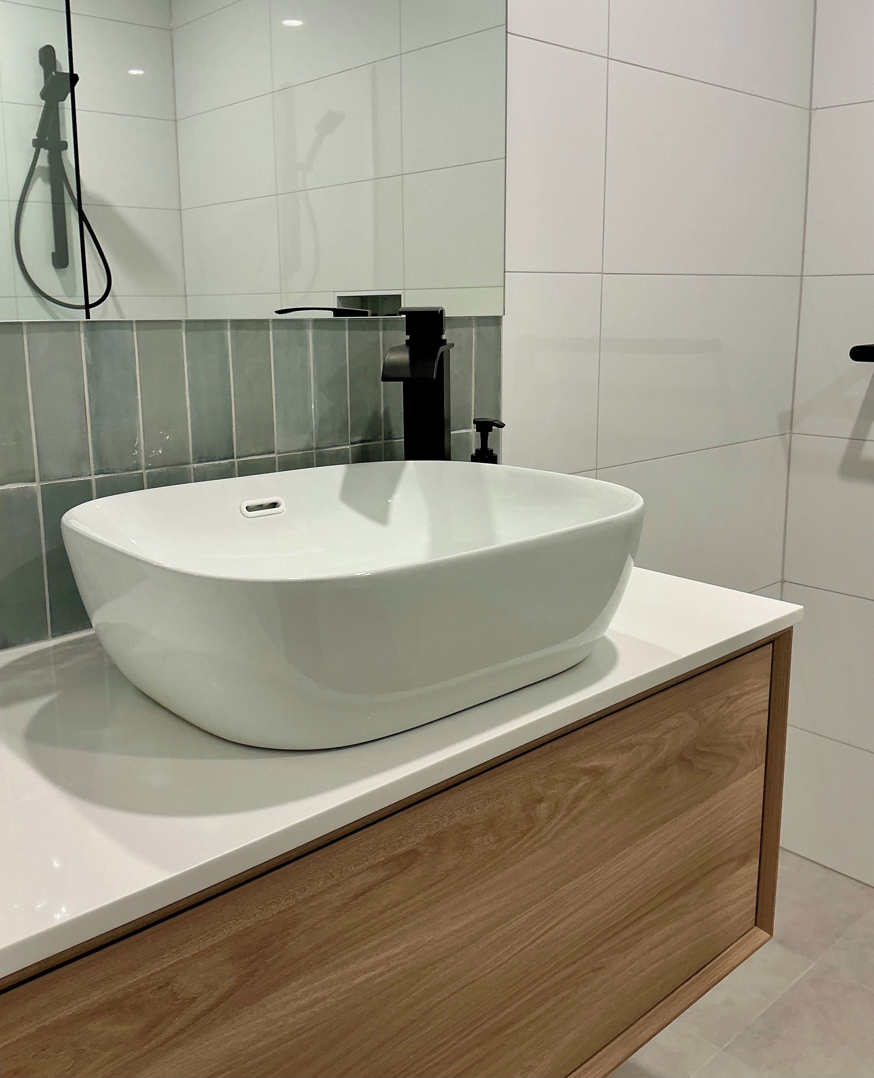 Un baño moderno con un lavamanos blanco de diseño, un grifo negro y un mueble de madera debajo.