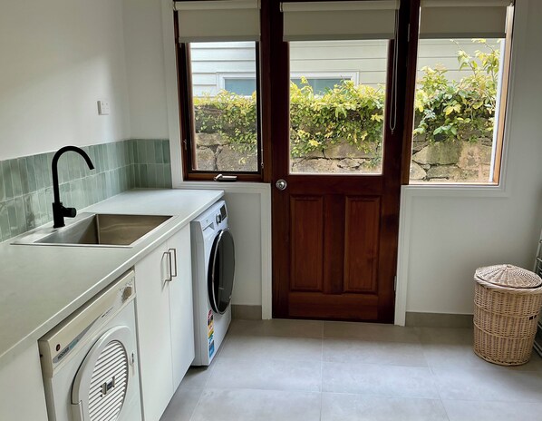 A compact kitchen with a built-in washer and dryer, a sink, and a window with a view of greenery outside.