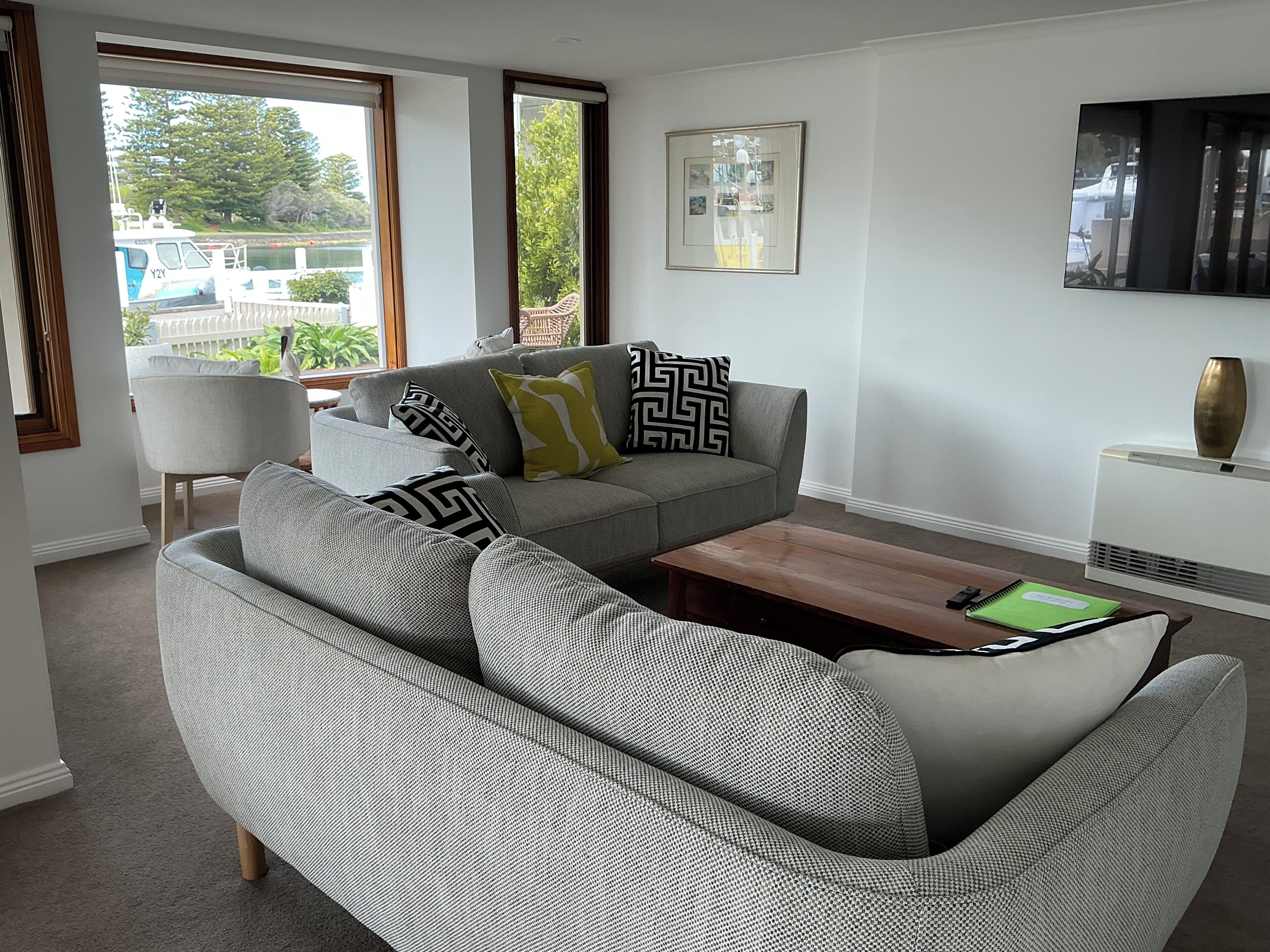 A modern living room with a grey sofa, patterned cushions, a wooden coffee table, and a framed picture on the wall.