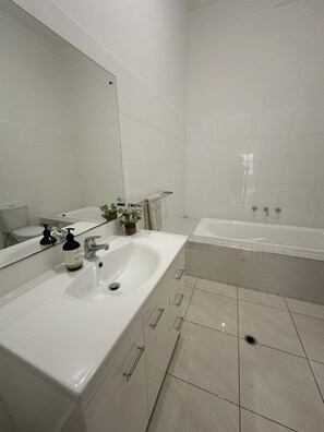 A modern bathroom with a large mirror, a white sink, a bathtub, and a toilet. - Esplanade Beach House with beautiful sea views (Semaphore)