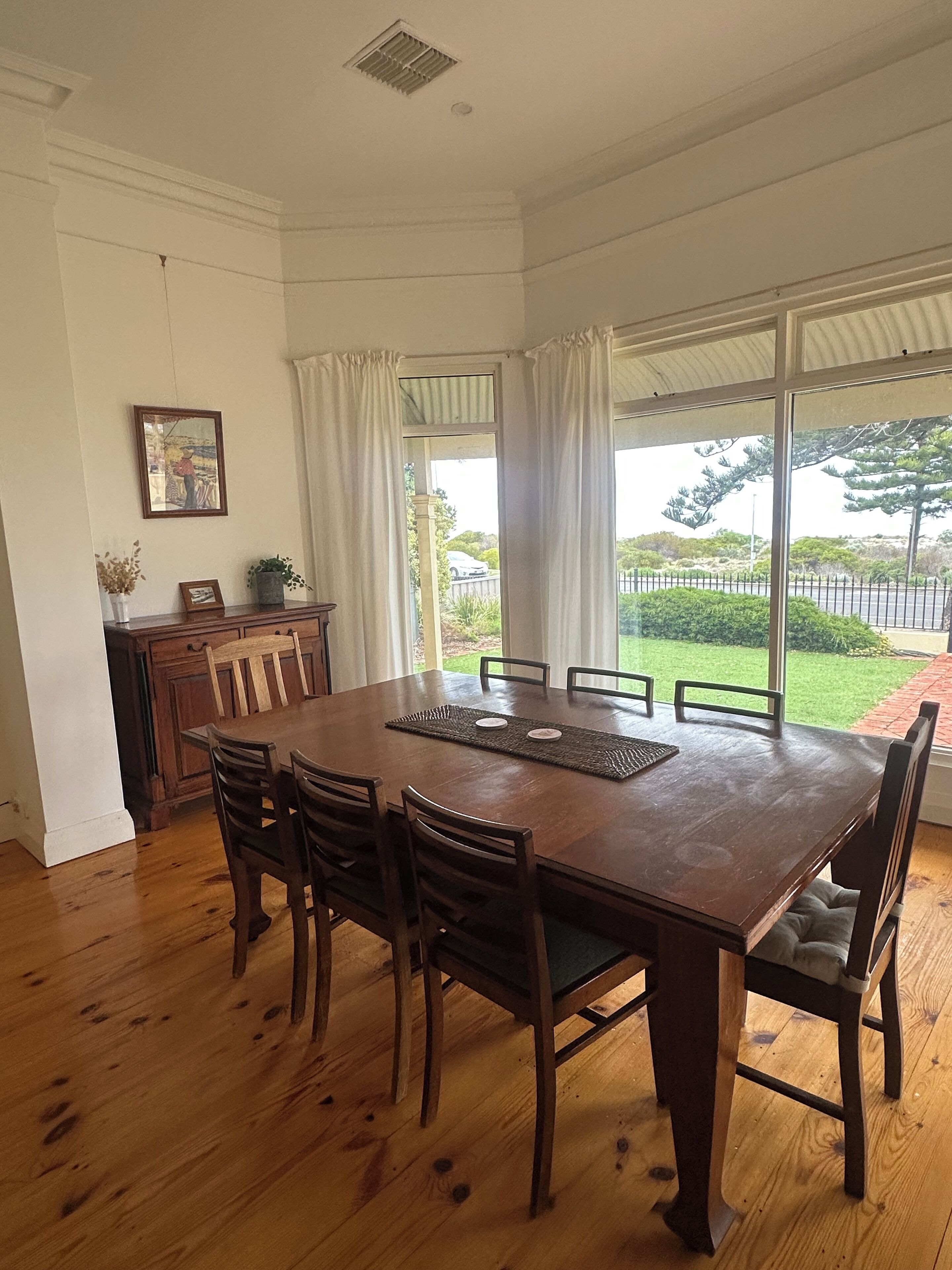 Un coin repas avec une grande table en bois, six chaises et une vue sur un jardin grâce à de grandes fenêtres.