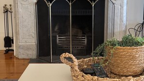A fireplace with a marble mantle, a woven basket with plants, and a white table in a room with wooden flooring. - Esplanade Beach House with beautiful sea views (Semaphore)