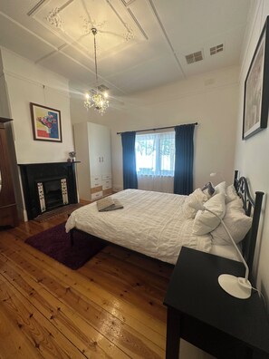 A bedroom with a large bed, a fireplace, a chandelier, and a window with curtains. - Esplanade Beach House with beautiful sea views (Semaphore)