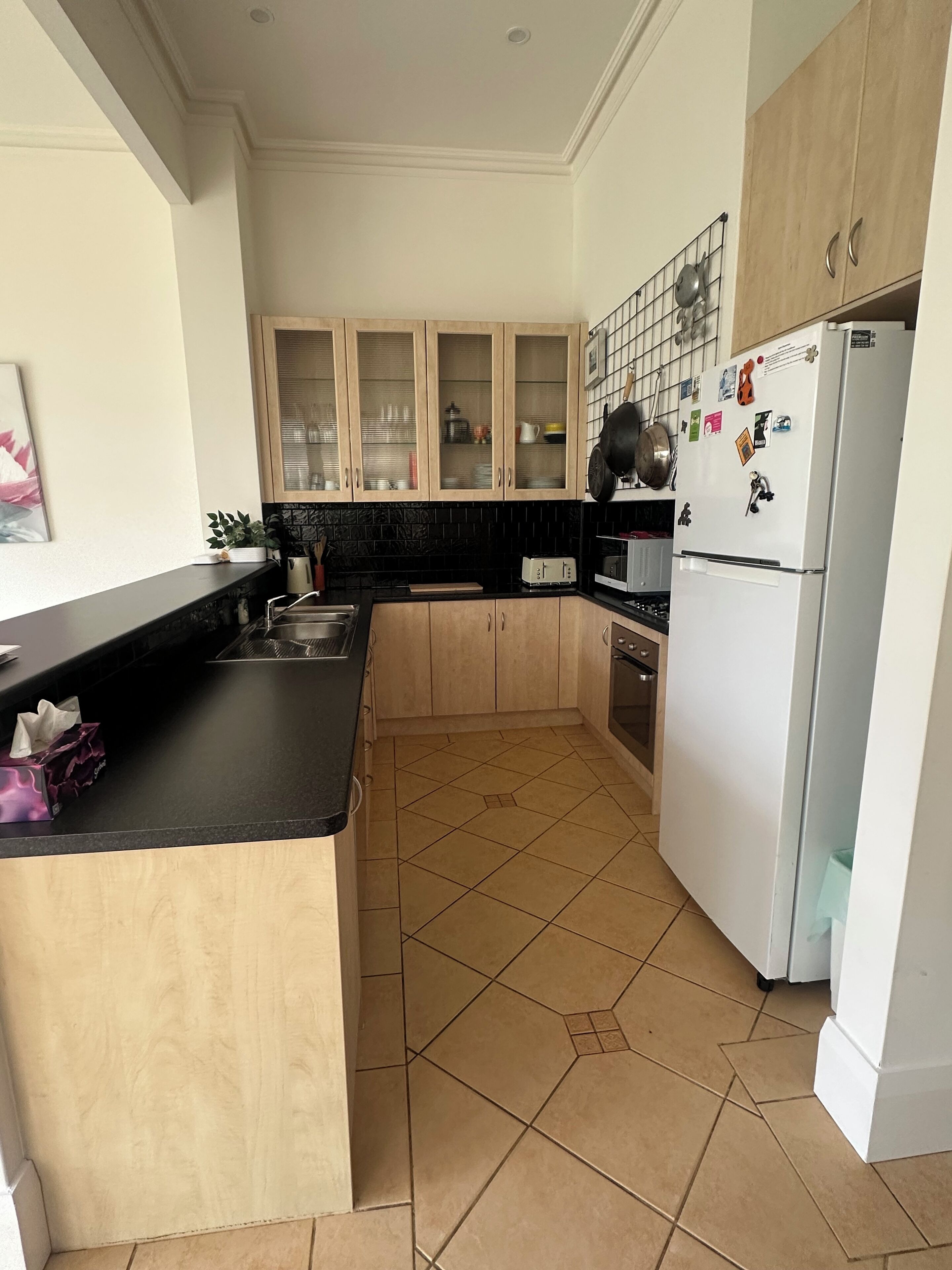 Una cocina con encimera negra, armarios de madera, refrigerador blanco y piso de baldosas.