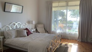 A neatly arranged bedroom with a bed, bedside tables, a chair, and a large window with curtains. - Esplanade Beach House with beautiful sea views (Semaphore)