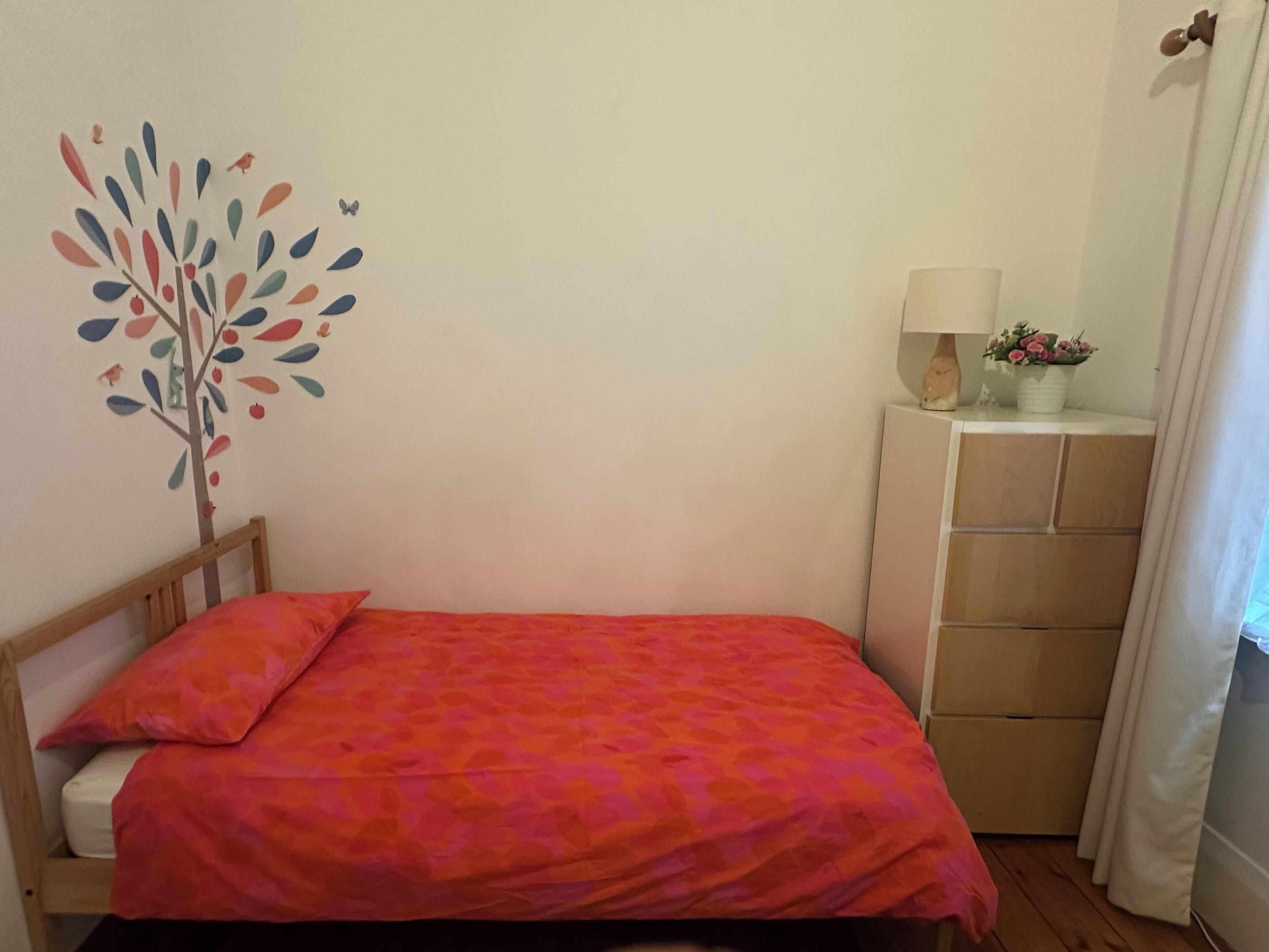 A small bedroom with a bed, a dresser, a wall decoration, and a lamp.