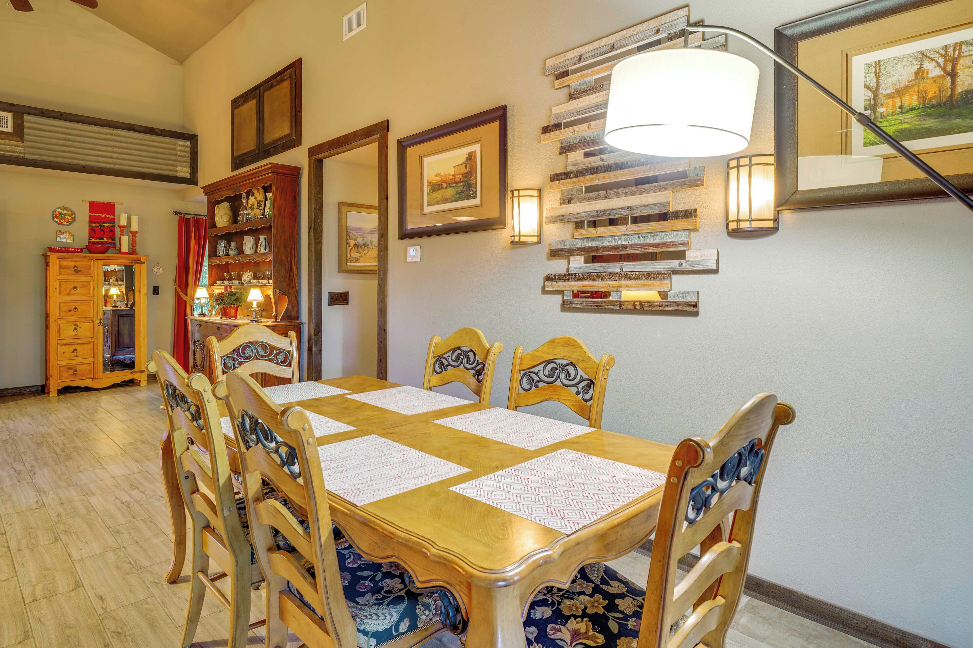 A dining area with a wooden table and chairs, a red cabinet, and wall-mounted shelves with books and framed pictures.