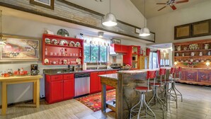A kitchen with red cabinets, a wooden island, bar stools, and a large window with curtains.