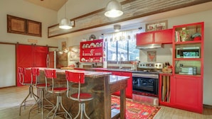 A kitchen with red cabinetry, a central island with stools, a stove, and a refrigerator.