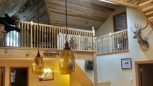 A dining area with a wooden table and chairs, a hanging light fixture, and a staircase leading to an upper level.