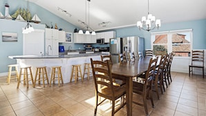 A spacious kitchen with a central island, wooden stools, and a dining table with chairs.