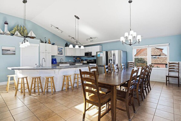 A spacious kitchen with a central island, wooden stools, and a dining table with chairs.