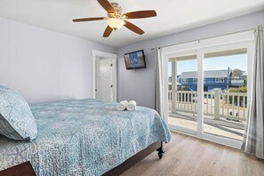 Un dormitorio con cama, ventilador de techo, puerta, ventana y vista al exterior.