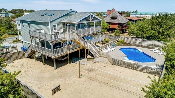 A two-story house with a deck, a swimming pool, and a fenced beach area.