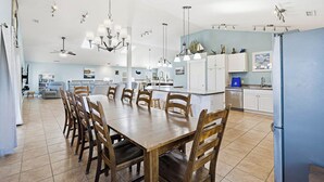 Uma cozinha espaçosa com área de jantar, destacando uma grande mesa de madeira e cadeiras, uma ilha central e luminárias modernas.
