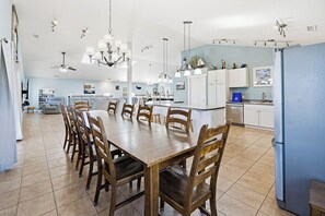 A spacious kitchen with a dining area, featuring a large wooden table and chairs, a central island, and modern lighting fixtures.