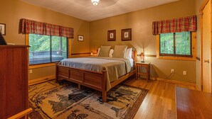 A bedroom with a wooden bed, two bedside tables, a rug, and plaid window valances.