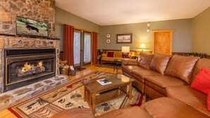 A cozy living room with a stone fireplace, leather sofa, and a television mounted on the wall.