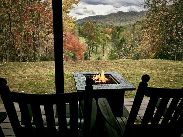 A covered outdoor seating area with a fire pit, overlooking a forested hillside.
