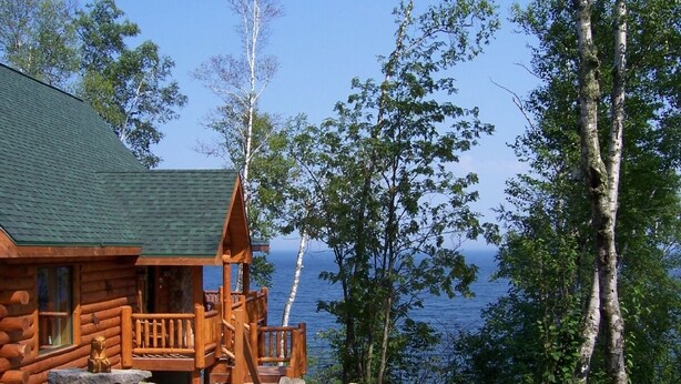 A log cabin with a porch and a view of the lake. - Lake Superior Luxury Log Home, Sauna, Waterfront, Amazing Views (Two Harbors)