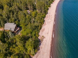 An aerial view of a beach with a house and dense forest.