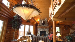 A log cabin interior with a stone fireplace, wooden furniture, and a hanging light fixture. - Lake Superior Luxury Log Home, Sauna, Waterfront, Amazing Views (Two Harbors)