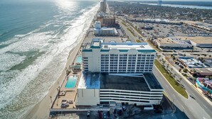 Een hotel met zwembad, parkeerplaats en uitzicht op het strand.