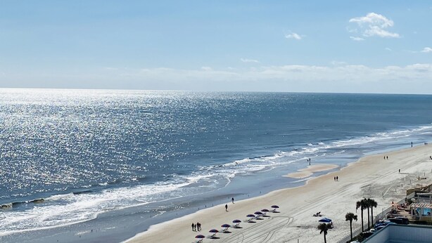 A beach with a clear sky, sandy shore, and umbrellas. - Daytona Beach 12th Floor Oceanview With Spectacular Views (Daytona Beach)