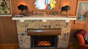 A stone fireplace with a fire, a Native American headdress, and a 'WELCOME' sign above it. - SPECTACULAR LODGE ON PRIVATE RANCH. PERFECT FOR SMALL AND LARGE GATHERINGS! (LEAKEY)