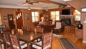 A spacious living room with a wooden dining table, multiple chairs, a fireplace, and a television. - SPECTACULAR LODGE ON PRIVATE RANCH. PERFECT FOR SMALL AND LARGE GATHERINGS! (LEAKEY)