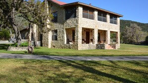 A stone house with a red roof, a covered porch, and a view of a hilly landscape. - SPECTACULAR LODGE ON PRIVATE RANCH. PERFECT FOR SMALL AND LARGE GATHERINGS! (LEAKEY)