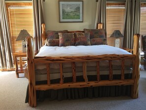 A wooden bed with a white mattress and patterned pillows, flanked by curtains and a framed picture on the wall.