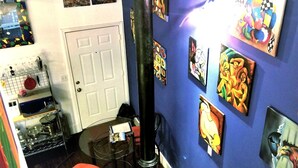 A room with a blue wall adorned with various artworks, a white door, a glass table with a chair, and kitchen items on shelves. - The Gallery Getaway in the Heart of Historic, Riverfront Wilmington!  (Wilmington)