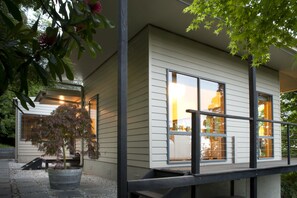 Een modern huis met grote ramen, een houten terras en een plant in een pot.