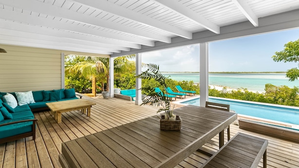 A covered outdoor area with a wooden deck, a wooden table, a teal sofa, and a view of the ocean. - Sueno De Mar: Beachfront Villa for 10 (Hartswell)