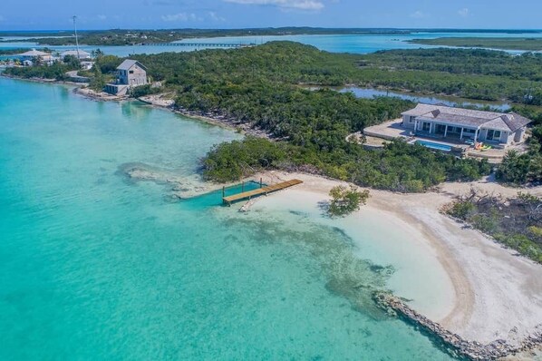 Een landgoed aan de kust met een groot huis, een steiger en een heldere turquoise zee.