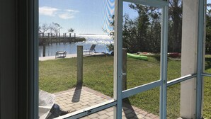 A view through a glass door to a patio area with a grassy lawn, a small pool, and a few kayaks. - Private Oceanfront Cottage with dockage, pool just minutes to Key West! (Cudjoe Key)