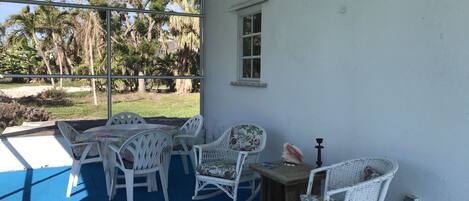 A covered patio area with white wicker furniture and a view of palm trees and grass.