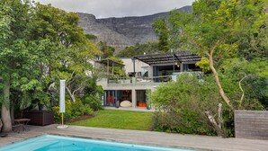 Una casa a due piani con piscina, immersa nel verde con montagne sullo sfondo.