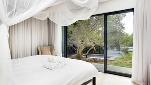 Una camera da letto con un letto grande, tende leggere e vista sul verde circostante.