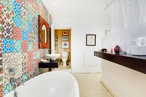 A modern bathroom with a white bathtub, a sink, and a toilet. The walls are decorated with colorful tiles. - Solar-Powered Table Mountain Retreat, Kid-Friendly Space with Lush Garden & Pool (Cape Town)