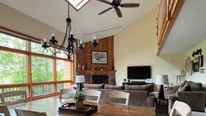 A spacious living area with a dining table, chairs, a fireplace, a television, and a balcony with large windows. - A Breath of Fresh Air—Weekend Plans at the Timberview (Carroll)