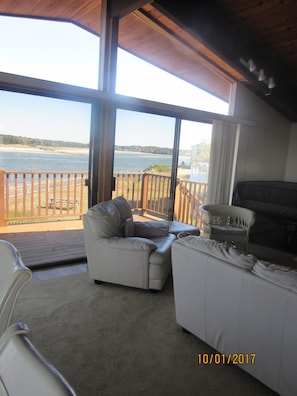 Enjoy the serene view of the lake from the spacious living area, featuring a comfortable sofa and a wicker chair on the deck.