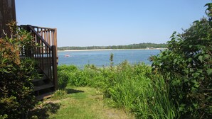 A wooden deck overlooking a calm body of water with a distant shoreline and a small red building. - The Waterfront Deckhouse-Pine Point Beach Waterfront Property (Scarborough)