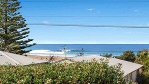 A coastal view with a beach, ocean, and a building with a sloped roof. - MYSTIC WAVES | WIFI , Pet Friendly | Accom Holidays (WAMBERAL)