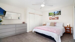 A bedroom with a bed, bedside tables, a wardrobe, a ceiling fan, and a window with a view. - MYSTIC WAVES | WIFI , Pet Friendly | Accom Holidays (WAMBERAL)