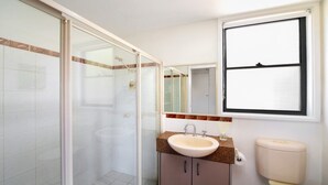 A bathroom with a glass shower enclosure, a sink with a mirror, and a toilet. - MYSTIC WAVES | WIFI , Pet Friendly | Accom Holidays (WAMBERAL)
